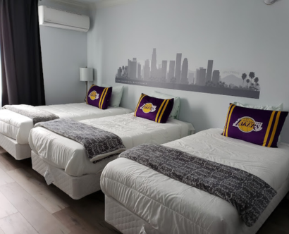 Three beds adorned with Lakers-themed pillows in a cozy room at Hometel Suites, offering affordable and comfortable stays.